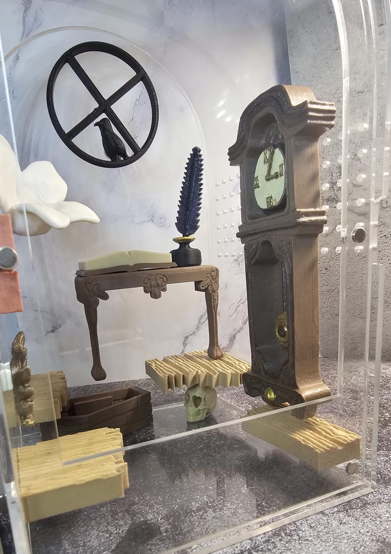 May include: A miniature room display with a wooden table, a clock, a skull, and a book. The room is enclosed in a clear acrylic case.