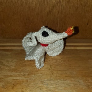 Op de afbeelding: Witte gehaakte geestfiguur met een zwart oog, een rode kraag en een oranje-gele neus.