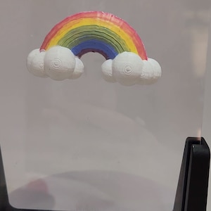 May include: A rainbow with clouds, painted in red, orange, yellow, green, blue, and purple, is displayed in a clear acrylic box with a black base.