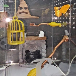 May include: A clear acrylic box with a rotating base, featuring a miniature Harry Potter themed scene. The scene includes a Sorting Hat, a golden cage, a broomstick, a cauldron, and a golden snitch.