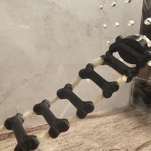 May include: A black bone-shaped ladder made of 3D printed plastic, strung together with a natural twine rope.