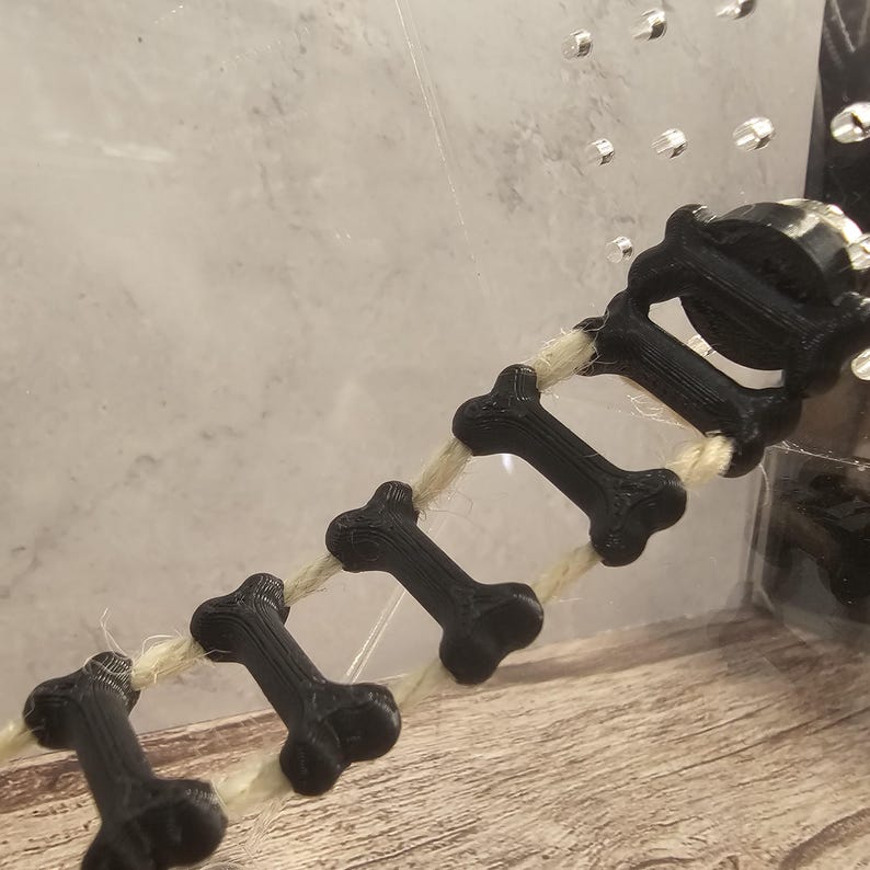 May include: A black bone-shaped ladder made of 3D printed plastic, strung together with a natural twine rope.