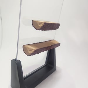 May include: Two brown wooden logs with a textured surface, mounted on a clear acrylic frame with a black stand.