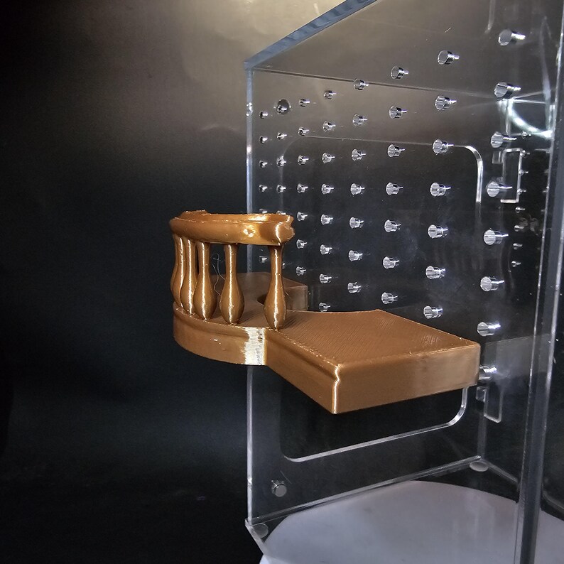 Puede incluir: Un balc&oacute;n en miniatura de color marr&oacute;n impreso en 3D con una barandilla y una plataforma. El balc&oacute;n est&aacute; unido a una pared de acr&iacute;lico transparente.