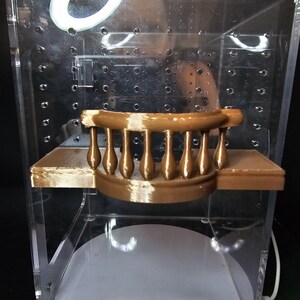 Puede incluir: Una barandilla de balc&oacute;n de pl&aacute;stico marr&oacute;n impresa en 3D con una plataforma plana. La barandilla est&aacute; hecha de un material liso, similar al pl&aacute;stico, y tiene una forma redondeada. La plataforma es plana y tiene una superficie texturizada.