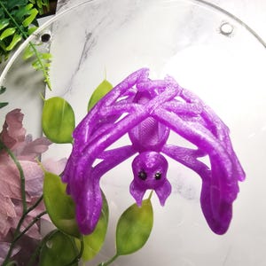 May include: A purple 3D printed spider with a detailed design. The spider is hanging upside down with its legs spread out.