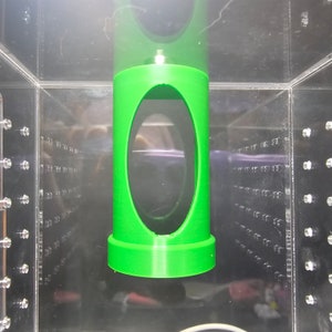 May include: A green plastic cylinder with a large oval opening in the center. The cylinder is suspended in a clear plastic container.