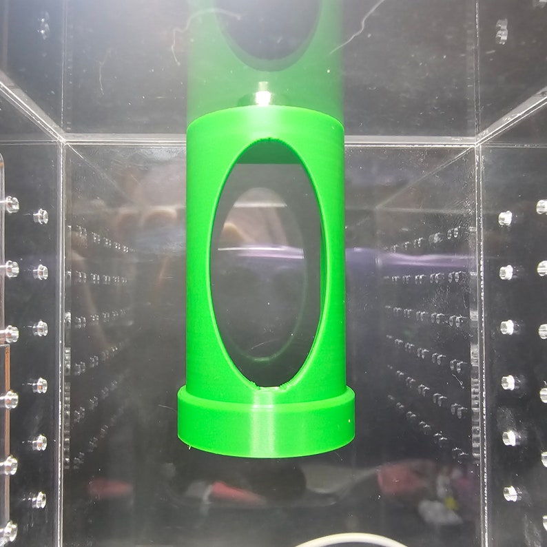 May include: A green plastic cylinder with a large oval opening in the center. The cylinder is suspended in a clear plastic container.