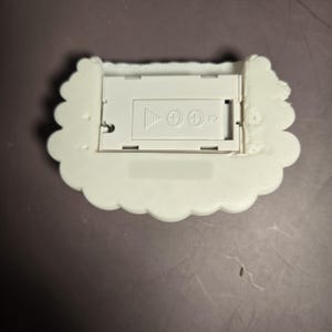 Peut inclure: Un compartiment &agrave; piles blanc en forme de nuage avec une ouverture rectangulaire. Le compartiment comporte des symboles plus et moins, et une fl&egrave;che indiquant le sens d'insertion des piles. Les bords du nuage sont festonn&eacute;s.