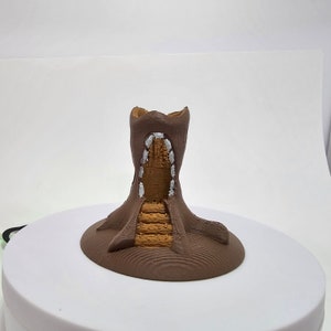 May include: A 3D printed miniature tree stump with a staircase leading up to a hollow opening at the top. The stump is painted brown with white accents.