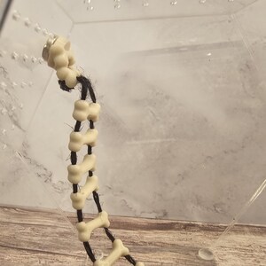 May include: A white bone-shaped charm bracelet with black string and a magnetic clasp.