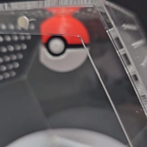 Puede incluir: Una vitrina de pl&aacute;stico transparente con una Pok&eacute;bola roja y blanca en su interior. La vitrina est&aacute; hecha de acr&iacute;lico transparente y tiene una forma hexagonal.