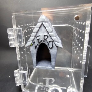 May include: A small gray dog house with the word "ZERO" written on the front. The dog house is inside a clear acrylic display box.