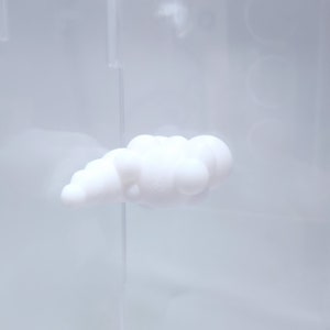 May include: A white cloud-shaped object made of soft, squishy material. The object is displayed in a clear acrylic case.
