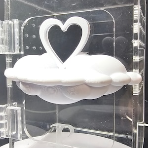 May include: A white 3D printed cloud with a heart-shaped cutout on top. The cloud is displayed in a clear acrylic box.