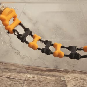 May include: A black and orange dog bone chew toy chain. The chain is made of alternating black and orange bone shapes connected by black string.