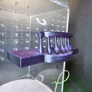 Puede incluir: Un modelo de puente impreso en 3D en color morado y negro con una barandilla y seis pilares. El modelo est&aacute; sentado en una plataforma.