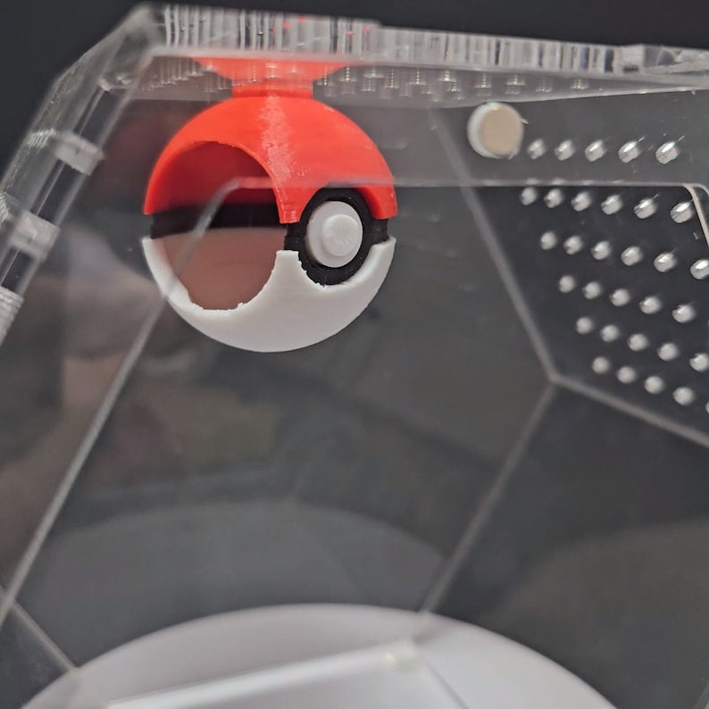 Puede incluir: Un juguete Pokeball rojo y blanco dentro de una vitrina hexagonal de pl&aacute;stico transparente.