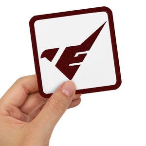 Könnte beinhalten: Ein weißer quadratischer Patch mit rotem Rand. Der Patch zeigt einen stilisierten Vogel mit einem rot-weißen Design. Der Vogel blickt nach rechts.