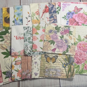 May include: A collection of decorative paper napkins with floral and nature-inspired designs. The napkins feature various patterns, including butterflies, flowers, and birds. Some napkins have text, such as "I am brave" and "Mainen Blume".