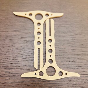 May include: A wooden cutout of the letter I with a series of holes along the vertical line. The cutout is light brown and has a smooth finish.