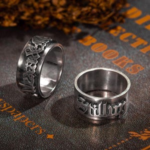 Op de afbeelding: Twee zilveren ringen met gegraveerde letters. De ring aan de linkerkant zegt "Space" en de ring aan de rechterkant zegt "Silly".