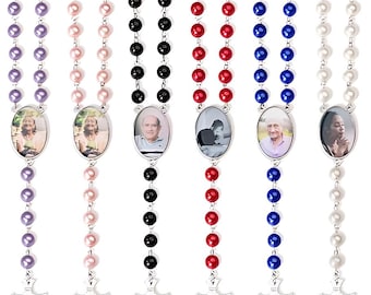 May include: Six different colored rosary necklaces with a photo charm. The rosaries are purple, pink, black, red, blue, and white. Each charm features a different photo of a person.