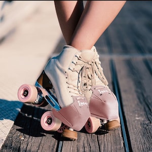 Puede incluir: Un par de patines blancos con protectores de dedos rosas. Los protectores de dedos tienen la palabra "love" escrita en ellos.