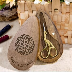May include: A wooden box with a carved shamrock design and the text "Mary's scissors". The box is open and contains a pair of gold-coloured scissors with a bird design.