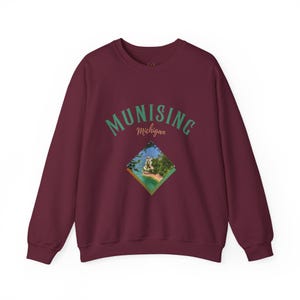 May include: Burgundy sweatshirt with the word "MUNISING" in green arched text above a diamond-shaped image of a coastal landscape. The word "Michigan" is below the word "MUNISING".