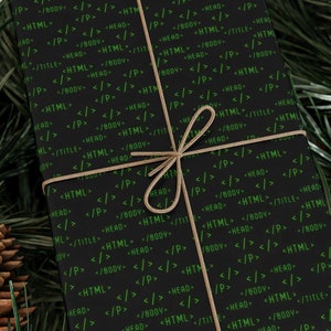 Op de afbeelding: Een zwarte cadeaudoos verpakt in papier met een groen codepatroon. De doos is vastgebonden met touw en ligt op een bed van groene dennennaalden.