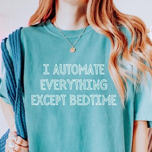 Op de afbeelding: Tealkleurig T-shirt met de witte tekst "I AUTOMATE EVERYTHING EXCEPT BEDTIME". Het shirt heeft een casual stijl, waarschijnlijk gemaakt van zacht materiaal. De afbeelding suggereert een ontspannen, alledaags kledingstuk.