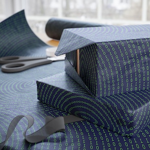 May include: A stack of three gift boxes wrapped in blue and green wrapping paper with a binary code pattern. The boxes are wrapped in a circular pattern.