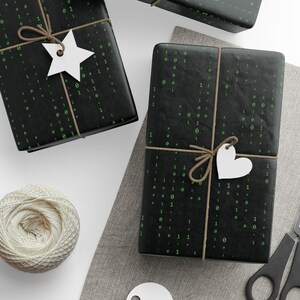 Könnte beinhalten: Drei schwarze Geschenkboxen mit grünen 1er und 0er darauf gedruckt. Die Boxen sind mit Schnur gebunden und mit weißen Papiersternen und Herzen verziert.