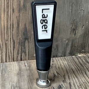 May include: Black plastic beer tap handle with a white label that says "Lager" and a silver base.