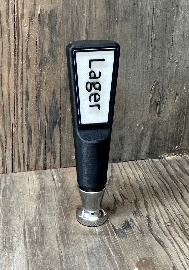 May include: Black plastic beer tap handle with a white label that says "Lager" and a silver base.