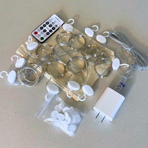 May include: A set of string lights with a remote control, power adapter, and mounting clips. The lights are on thin silver wires, coiled into circles. The remote is black and white. A small bag of clear clips is also included.