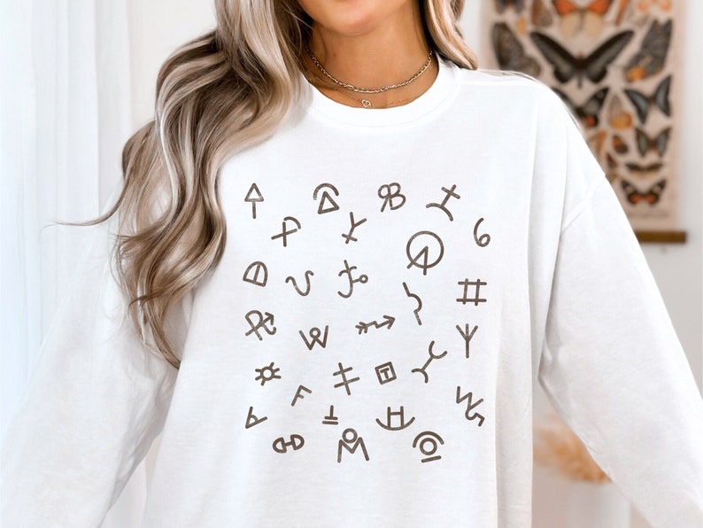 Op de afbeelding: Witte longsleeve sweatshirt met een bruine grafische afbeelding van verschillende symbolen en karakters die in een cirkel zijn gerangschikt.