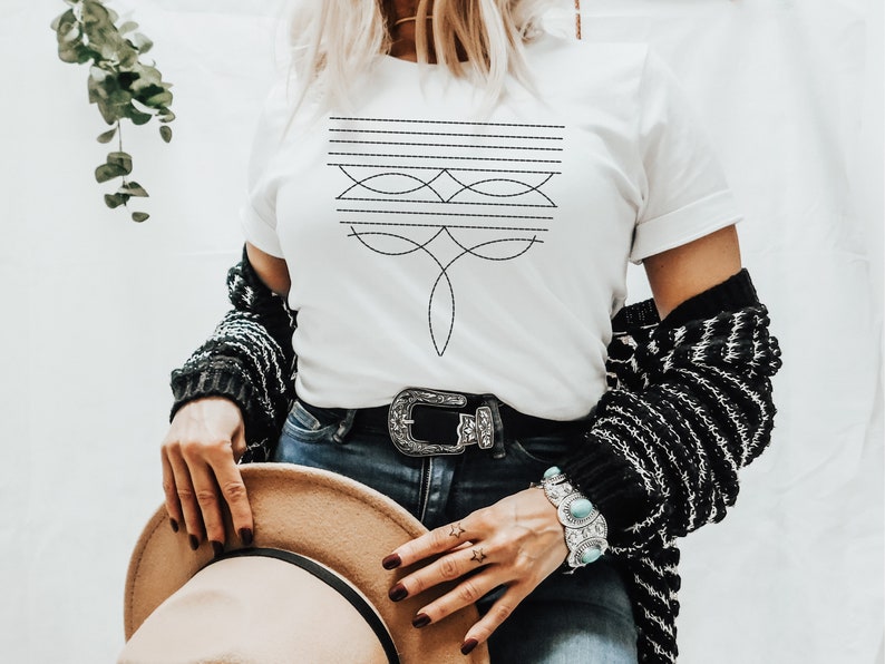 Puede incluir: Una camiseta blanca con un dise&ntilde;o geom&eacute;trico negro en la parte delantera. El dise&ntilde;o presenta una serie de l&iacute;neas horizontales y l&iacute;neas curvas que crean un patr&oacute;n sim&eacute;trico.