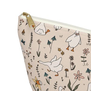 May include: A pink canvas zippered pouch with a white goose and floral pattern. The pouch has a gold zipper.