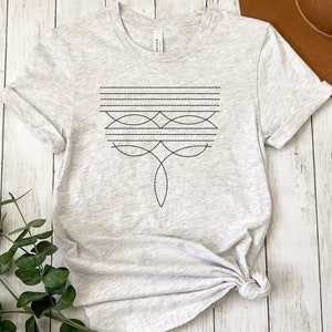 Puede incluir: Una camiseta gris jaspeada con un dise&ntilde;o geom&eacute;trico negro en la parte delantera. El dise&ntilde;o presenta una serie de l&iacute;neas y curvas.