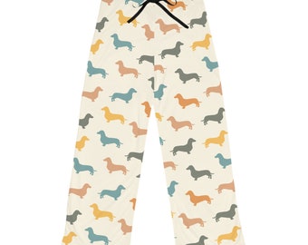 May include: Cream-colored pajama pants with a repeating pattern of dachshund dogs in various colors, including blue, orange, yellow, and gray. The pants have a black drawstring at the waist.