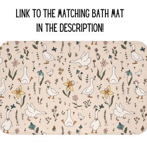 May include: A beige bath mat with a repeating pattern of white geese, flowers, and leaves. The geese are facing different directions and have small black eyes. The flowers are in shades of pink, yellow, and blue. The leaves are green.