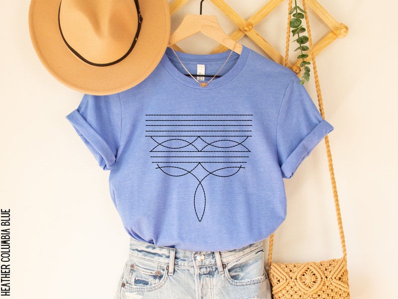 Puede incluir: Una camiseta azul cielo jaspeada con un dise&ntilde;o geom&eacute;trico en negro. El dise&ntilde;o presenta una serie de l&iacute;neas horizontales y formas curvas.