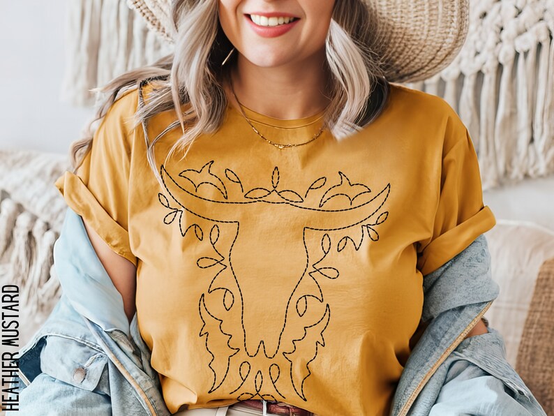 May include: A mustard yellow t-shirt with a black embroidered design of a stylized bull's head with floral accents.
