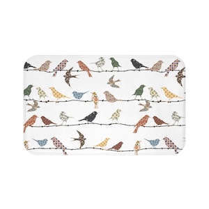 May include: A white bath mat with a repeating pattern of colorful birds perched on branches. The birds are made of patchwork fabric with floral designs.