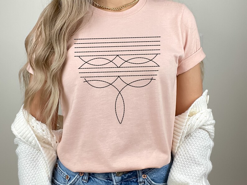 Puede incluir: Una camiseta rosa con un dise&ntilde;o geom&eacute;trico en hilo negro. El dise&ntilde;o presenta una serie de l&iacute;neas horizontales y l&iacute;neas curvas que crean un patr&oacute;n sim&eacute;trico.