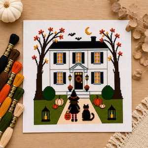 May include: A cross-stitch pattern on white fabric depicting a two-story house with black shutters, a witch figure, and a black cat on a path. The scene includes autumn trees, pumpkins, lanterns, and a crescent moon, accompanied by embroidery floss.