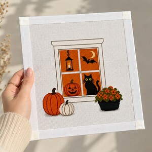 May include: A square needlepoint canvas featuring a Halloween scene with a window showing a lantern, a crescent moon, a bat, a jack-o'-lantern, and a black cat. In front of the window are two pumpkins and a potted plant with orange flowers.