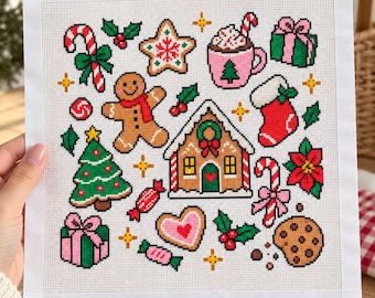 May include: A square needlepoint canvas featuring a grid of colorful Christmas-themed icons including a gingerbread house, a gingerbread person, a candy cane, a mug of hot cocoa, a Christmas tree, wrapped gifts, a stocking, and cookies.
